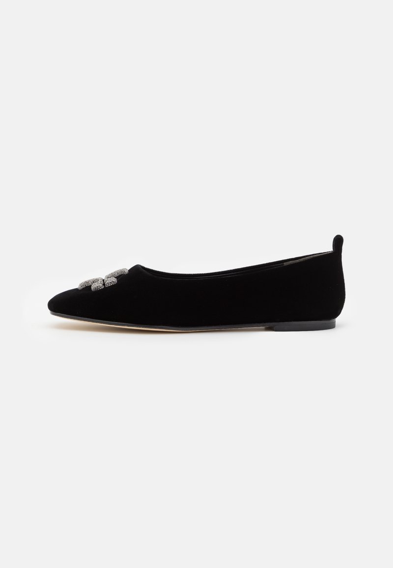 Chaussure plate en velours noir avec bout pointu et boucle en strass argenté sur fond blanc.