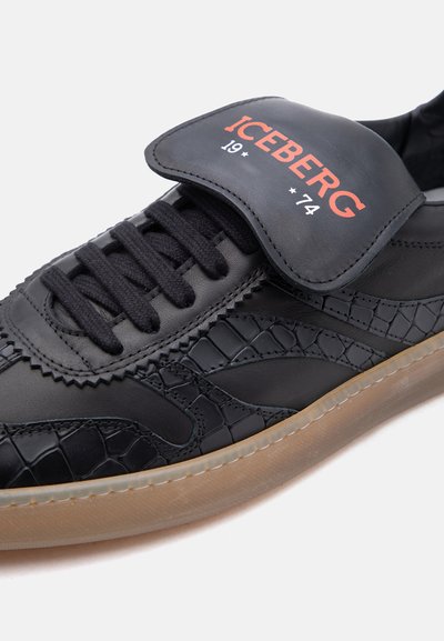 Baskets noires avec des panneaux texturés, lacets noirs, semelle en gomme, et un rabat marqué "ICEBERG 19 * 74" en texte rouge et blanc.