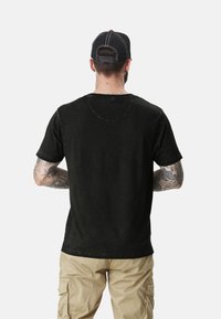 T-shirt noir à manches courtes avec une coupe décontractée et col rond. Tissu texturé avec un léger dégradé. Porté avec un pantalon cargo kaki.
