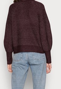Pull court en maille bordeaux avec texture côtelée, manches raglan et ceinture ajustée, associé à un jean taille haute bleu clair.