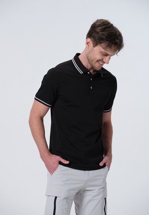 Camisa polo negra con ribete blanco en el cuello y las mangas, presenta una tapeta con tres botones y está hecha de un suave material de algodón.