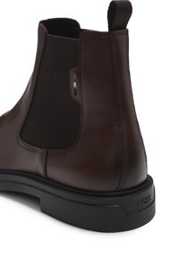 Botine Chelsea din piele maro închis, cu panouri elastice pe laterale, vârf rotund și talpă din cauciuc negru. Prezintă un logo subtil al brandului pe toc.