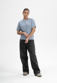 Hellblaues Baumwoll-T-Shirt mit kurzen Ärmeln, kombiniert mit schwarzen, weit geschnittenen Jeans. Angenehme Textur, lockere Passform und neutral gefärbte Fußbekleidung.