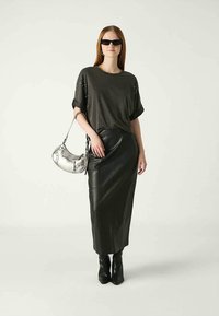 Black leather long skirt paired with a dark oversized t-shirt featuring metallic details. Model carries a silver handbag and wears sunglasses.