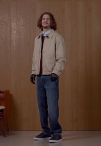 Bežna bomberska jakna, maroon pulover, modri džins, črne rokavice in sivi športni copati. Gladka tekstura, preprost dizajn in sproščen kroj.