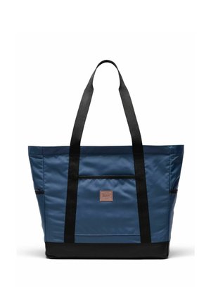 Sac fourre-tout bleu avec anses et base noires, poche frontale rectangulaire et petite étiquette de marque marron centrée sur le devant.