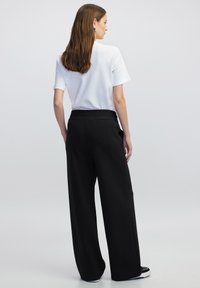 Zwarte wijde pantalons met een elastische tailleband, gecombineerd met een eenvoudig wit T-shirt met korte mouwen. Glad textuur van de stof, minimalistisch ontwerp.