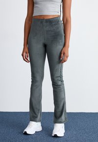 Corduroy flared pants in a muted green color, featuring a high waist, vertical ribbing, and a sleek design with side accents.