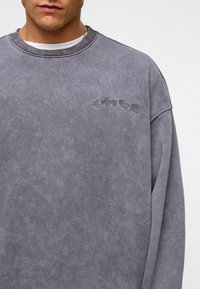 Grijze oversized sweatshirt met een zachte textuur, geribbelde kraag en geborduurde tekst op de voorkant. Heeft een relaxed fit en verlaagde schouders.