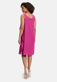 Fuchsiasfarbenes ärmelloses Kleid mit lockerer Passform, runder Rückseite und drapiertem Design; kombiniert mit silbernen Riemchenheels mit einem Regenbogenstreifenmuster.