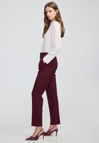 Bílá blůza s dlouhými rukávy a bordó kalhoty v konfekčním střihu. Blůza má hladký povrch, zatímco kalhoty mají klasický rovný střih.
