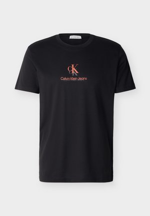 Μαύρο t-shirt με κοντά μανίκια και στρογγυλή λαιμόκοψη, με το λογότυπο "CK" και την επιγραφή "Calvin Klein Jeans" σε κόκκινο στο στήθος.