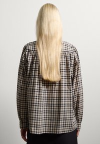 Long-sleeve shirt in beige and navy check pattern, featuring a loose fit, gathered shoulder seams, and buttoned cuffs.