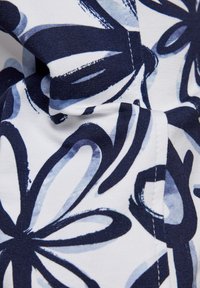Cotton fabric featuring a floral pattern in navy and light blue on a white background, with a smooth texture and soft drape.