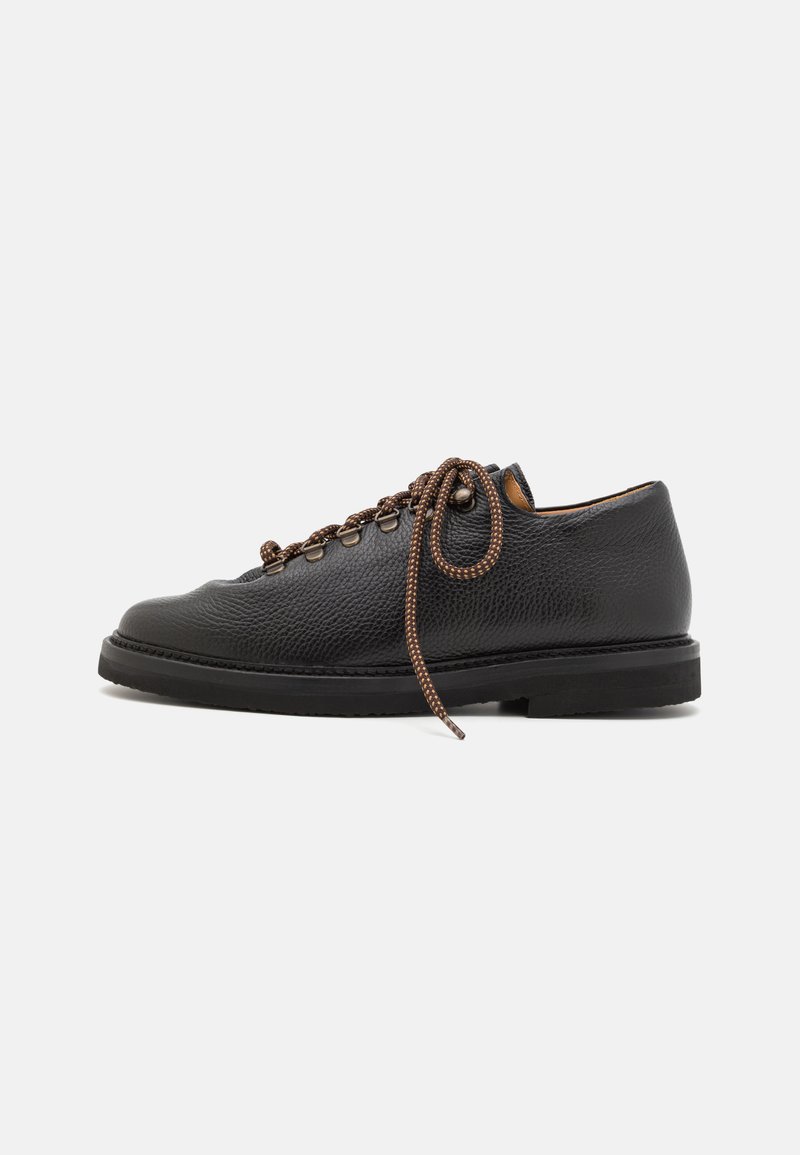 Chaussure en cuir noir avec une finition texturée, lacets marron et œillets en métal. Elle présente une silhouette basse et une semelle plate en caoutchouc.