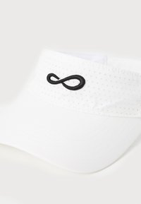 Hvid skygge med perforeret design, featuring et sort broderet uendelighedssymbol foran. Glat stof med struktureret skygge.