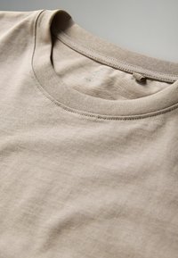 Beige crewneck t-shirt with fine ribbed collar and visible inside label reading "THE SET" in medium size.