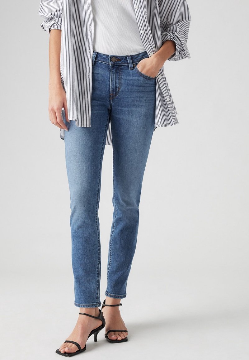 Jean skinny bleu clair à taille haute, en denim, associé à un débardeur blanc et une chemise à rayures noires et blanches à boutons.