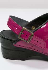 Fuchsia patent leather clog with adjustable buckle, black wooden platform, and textured inner lining, featuring black stitching accents.