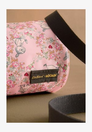Bolsa de tela rosa con patrones florales e ilustraciones de Moomin, con una correa oscura y una etiqueta negra que muestra "Cath Kidston x Moomin."