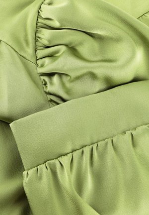 Groene satijnen stof met geplooide, gerimpelde secties die textuurrijke plooien en gladde, glanzende oppervlakken creëren.