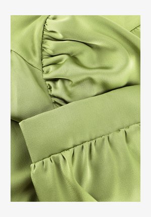 Groene satijnen stof met geplooide, gerimpelde secties die textuurrijke plooien en gladde, glanzende oppervlakken creëren.