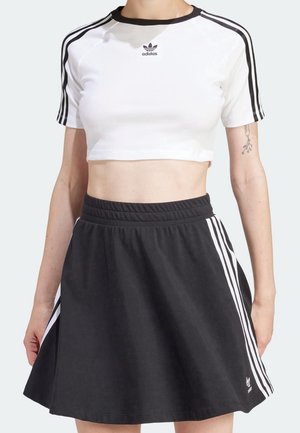 Hvid cropped top med sorte detaljer og tre sorte striber på ærmerne, parret med en sort flagrende nederdel med sidelommer og elastisk talje.