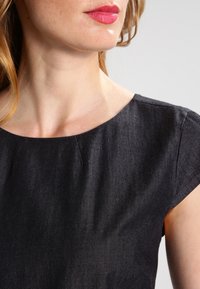 Musta farkkutoppi pyöreällä kaula-aukolla, lyhyillä hihoilla ja sile�ällä tekstuurilla. Sisältää hienovaraista ompelua ja istuvan leikkauksen.