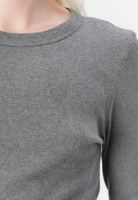 Gray ribbed long-sleeve top with a round neck, featuring a soft texture and a fitted shape. Visible stitching along the neckline.