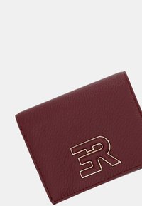 Portafoglio in pelle bordeaux con finitura texturizzata, caratterizzato da un evidente logo dorato sul davanti. Forma compatta e rettangolare.