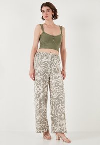 Olivově zelený žebrovaný cropped top s detailním knoflíkem, v kombinaci se světle vzorovanými širokými kalhotami v béžové a šedé barvě. Celý outfit doplňují sandály na podpatku.