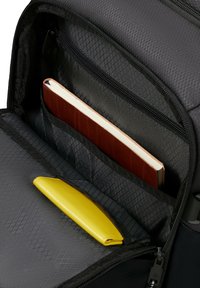 Mochila negra abierta para mostrar un bolsillo interior con un cuaderno marrón y una cartera amarilla dentro.