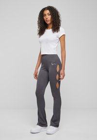 Pelēki riboti legingi ar izgrieztiem diamenta formas elementiem sānos, apvienoti ar pieguļošu baltu īso kreklu un baltām sporta apaviem.