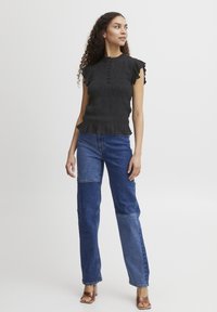 Haut smocké noir avec des manches courtes volantées et un col rond, associé à un jean en patchwork bleu, doté de panneaux en denim contrastés.