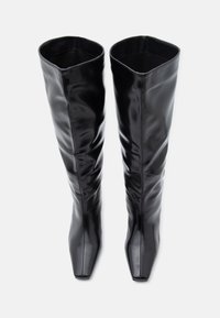 Μαύρες μπότες μέχρι το γόνατο από λείο, γυαλιστερό υλικό. Σχέδιο με τετράγωνη μύτη, με ρυτιδιασμένη υφή, άψογη κατασκευή και ψηλή σιλουέτα.