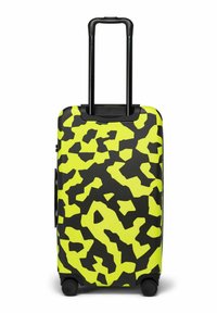 Valise rigide à motifs jaune vif et noir, avec une poignée télescopique noire extensible et quatre roues pivotantes noires.