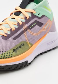 Scarpa da trail running Nike con un design viola, verde e arancione. Realizzata in materiale Gore-Tex e con suola in gomma texturizzata.
