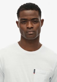 Witte katoenen t-shirt met een ronde halslijn en een borstzak voorzien van een klein merkje. De stof lijkt soepel en licht van gewicht.