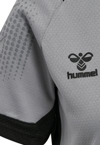 Szara sportowa rękawiczka z czarnym logo pszczoły i napisem „hummel”, z fakturowanymi wzorami kropek na górnej części ramienia.