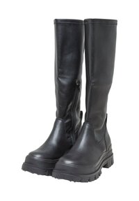 Paire de longues bottes en cuir noir avec fermeture éclair latérale et semelles épaisses en caoutchouc cranté sur fond blanc.