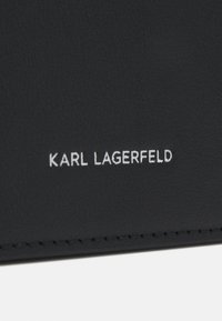 Čierna koža s textúrovaným povrchom, s embosovaným brandingom "KARL LAGERFELD" v bielej farbe. Prepracované švy viditeľné pozdĺž okrajov.