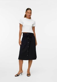 Jupe midi noire avec des boutons sur le devant et une taille nouée, assortie à un crop top blanc à manches courtes. Tissu lisse et design minimal.