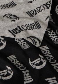 Țesătură tricotată neagră și gri cu un model abstract și textul "just cavalli", alternând între modele solide și dungi.