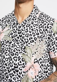 Kortärmad skjorta med ett svartvitt leopardmönster med rosa och gröna blommönster, knäppning framtill och spridningskrage.