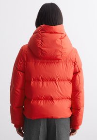 Czerwona puchowa kurtka z kapturem, z poziomymi przeszyciami, elastycznymi mankietami i gładkim, błyszczącym wykończeniem.