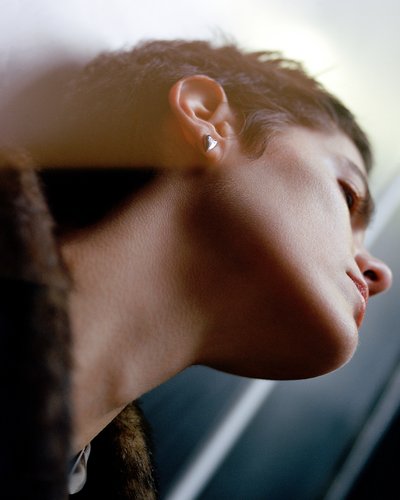 Gros plan d'une oreille avec une boucle d'oreille en argent en forme de cœur. La texture de la peau semble lisse, avec des cheveux courts et foncés partiellement visibles.