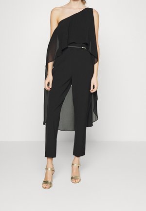 Černý overal s asymetrickým designem na jedno rameno, průhlednou vrstvou a přiléhavými kalhotami. Doplněný zlatými sandály na vysokém podpatku.