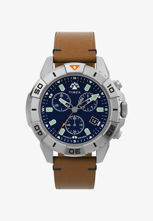 Ceas Timex cu carcasă din oțel inoxidabil, cadran albastru, brățară din piele maro, markere verzi luminescente și subcadrane pentru cronograf. Rezistent la apă până la 100 m.