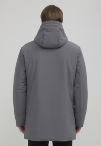 Giacca grigia imbottita con cappuccio, dalla texture liscia e dal taglio dritto, caratterizzata da un design minimalista e senza chiusure visibili.