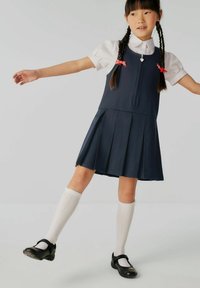 Rochie plisată bleu marin cu fermoar frontal, asortată cu o cămașă albă cu guler, ciorapi albi până la genunchi și pantofi Mary Jane negri.